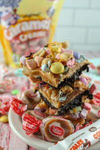 A caramel peanut butter cookie covered in a variety of candy with a cow tale and some caramel creams